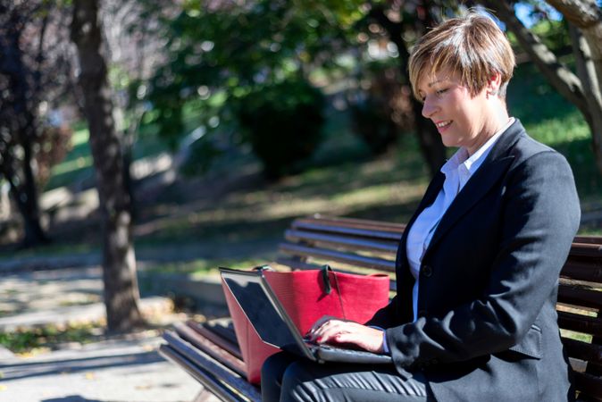 Professional woman sitting on park bench using laptop