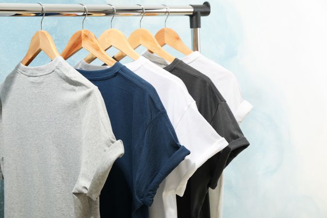 Rack with blank t-shirts on blue background, space for text
