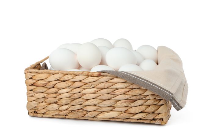 Chicken eggs in straw basket isolated on plain background
