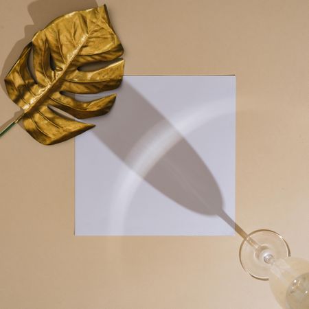 Shadow of wine glass with golden leaf and square paper on beige background