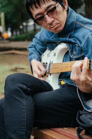 Man wearing denim jacket playing electric guitar in the park