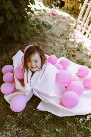 Happy girl wrapped in fabric with colorful balloons in garden