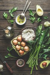 Preparing spinach ricotta stuffing with herbs, eggs and spices at dark wooden kitchen table. Cooking at home with fresh healthy ingredients. Top view.