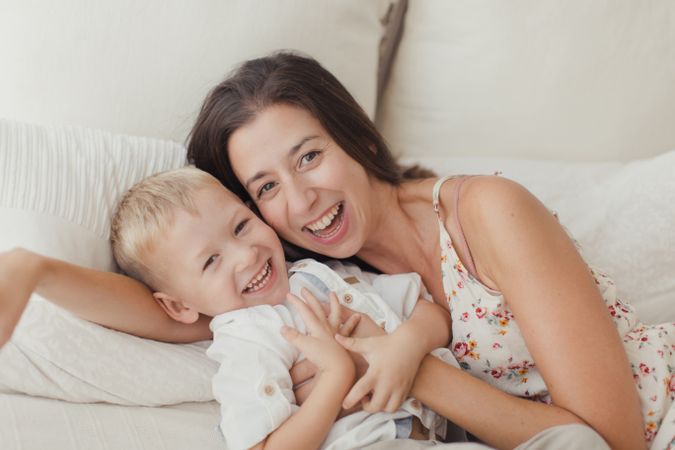 Mother ticking little son and laughing on bed
