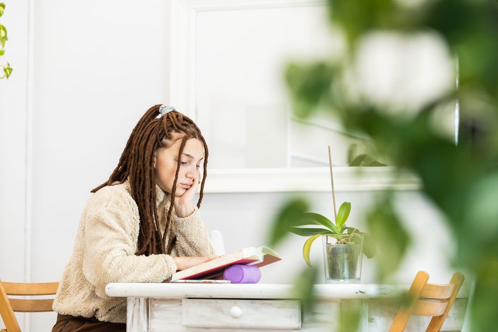Woman with braids reading a book while sitting at a table