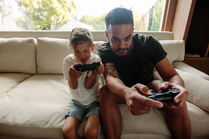 Father and son with video game controllers sitting on sofa