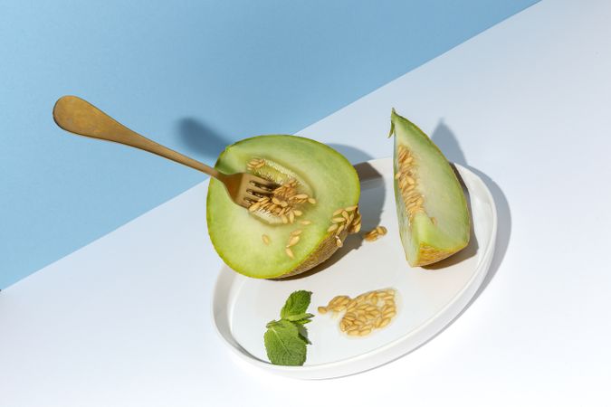 Sliced small melon on plate with spoon and fork