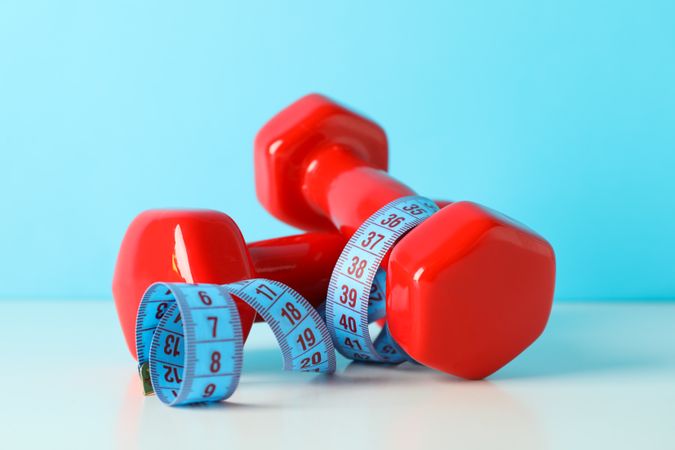 Dumbbells and measuring tape on table against blue background