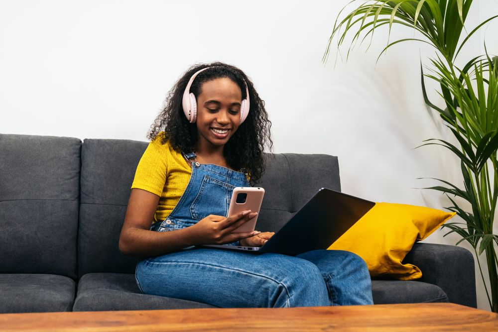 Young Black woman working with laptop and enjoying music at home