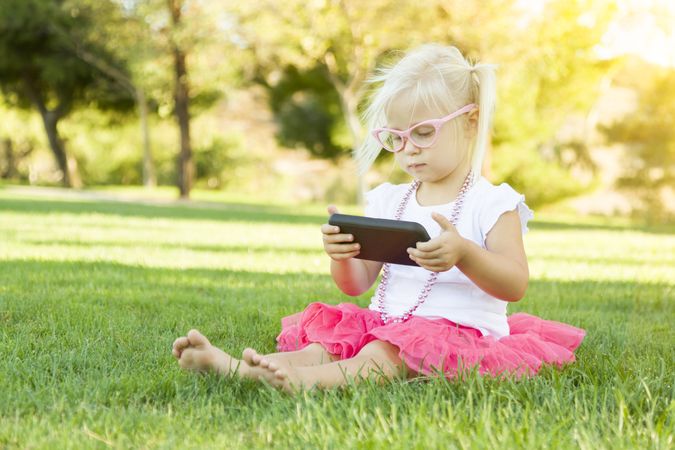 Little Girl In Grass Playing With Cell Phone