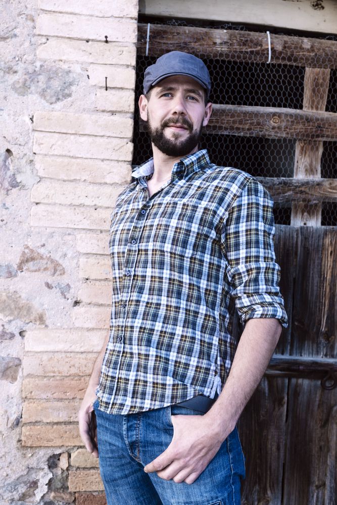 Casual man standing with his back against a brick wall while looking at camera