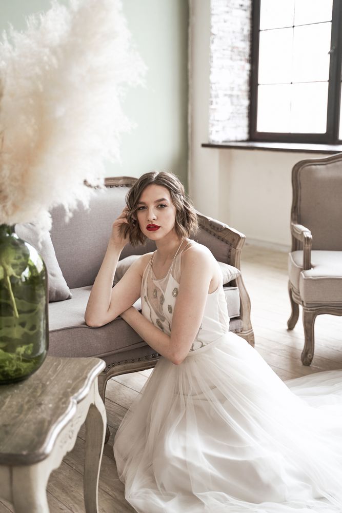 woman with red lips in white dress looking at camera while sitting on floor beside sofa