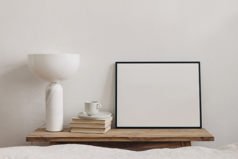 Cup of coffee, books and modern marble geometric lamp on vintage teak wooden bench next to mock up poster frame