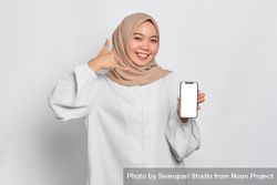 Asian Muslim woman presenting cell phone with mockup screen and hand making phone shape bxeXr0