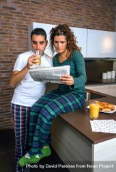 Couple in pajamas reading paper together in kitchen at breakfast 56rOd5