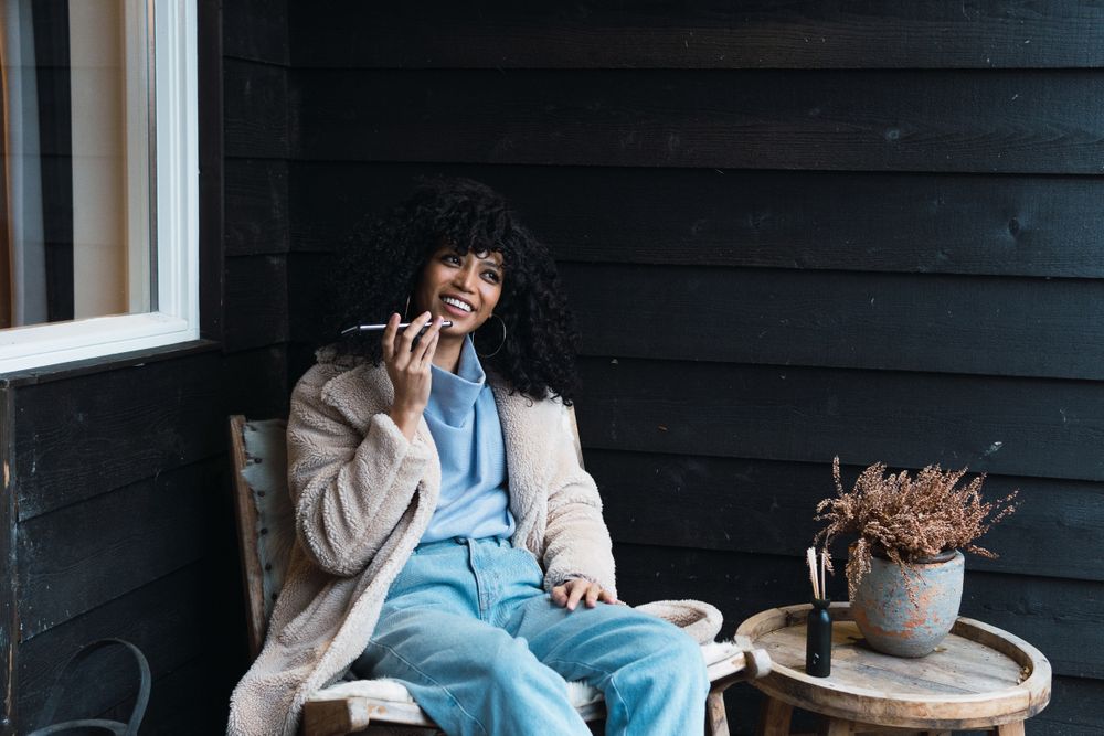 Cheerful Black woman recording voice message on terrace