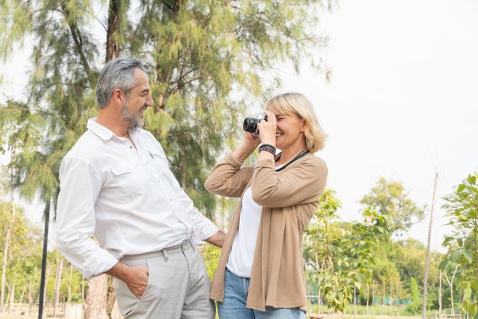 Happy mature woman taking picture of male friend in park