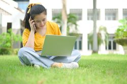 Young woman sitting on the lawn talking on the phone and using laptop.