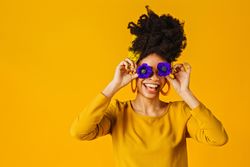 Smiling Black woman holding two purple flowers over her eyes