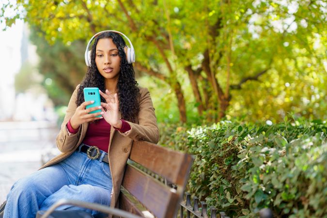 A Young Woman Is Relaxing in the Park While Enjoying Music on Her Smartphone Device