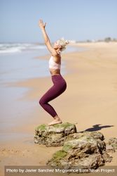 Woman practicing yoga pose reaching up on a Spanish beach bDzvy5
