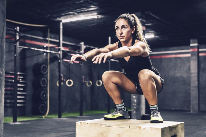 Athletic woman jumping on box to improve stamina in gym
