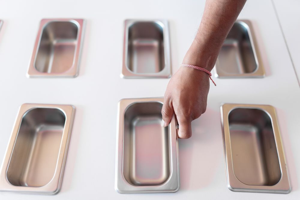 A hand of an ice-cream parlor worker is placing a clean metal tray