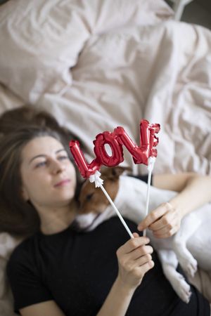 Woman lying on a bed holding her dog and a red love balloon above them both