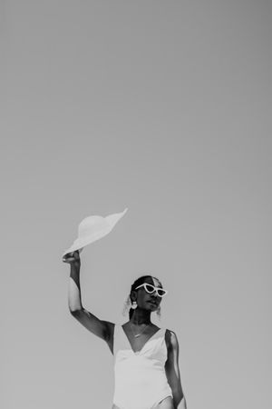 Grayscale image of woman wearing swimsuit blocking the sun with her hat