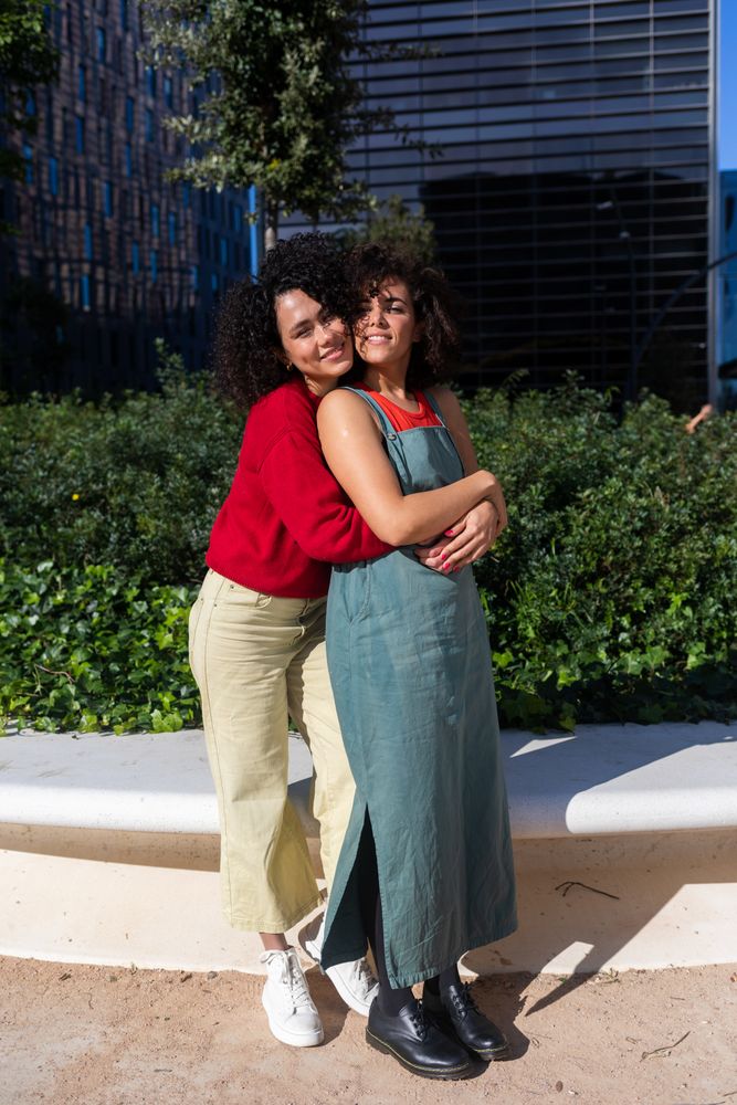 Female couple holding each other in city park with office buildings in background