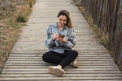 Dreamy woman sitting on boardwalk and writing in notebook in nature