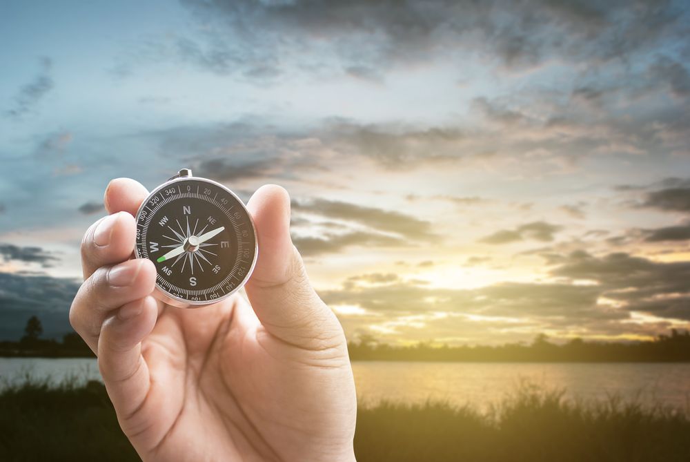 compass in hand on lagoon in the evening at sunset dark and noise background with dramatic clouds.