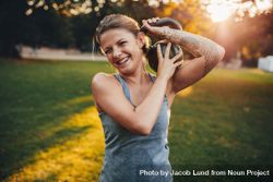 Portrait of happy young woman with kettlebell weights on her shoulder in the park 5zQoP0