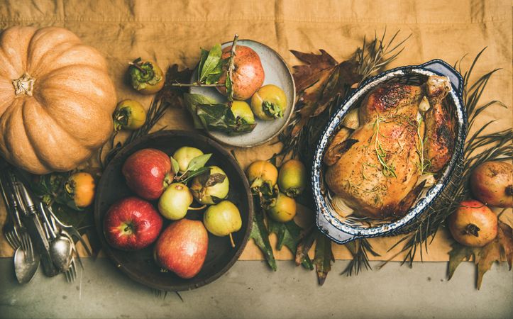 Roast turkey in decorative roasting pan, on table with fall leaves and fruit, horizontal composition