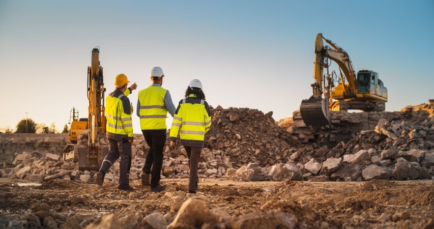 Construction Site With Excavators on Sunny Day: Diverse Team Of Male And Female Specialists Walking And Discussing Real Estate Project. Civil Engineer, Architect And Investor Talking, Using Tablet.