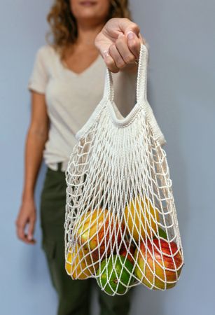 Unrecognizable woman holding reusable mesh bag with fruits inside