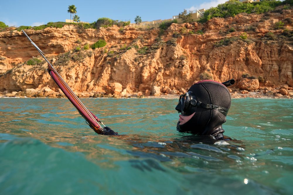 Man with speargun hunting in blue sea