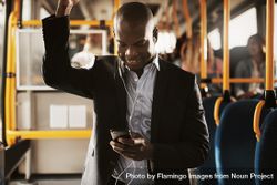 Man in business attire smiling at his phone on public transport bGzgl4