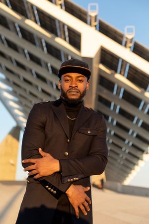 Portrait of stylish Black man standing outdoors with arms crossed over him in a sunny day