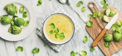 Brussels sprout soup, garnished with fresh sprouts, next to wooden board, wide composition
