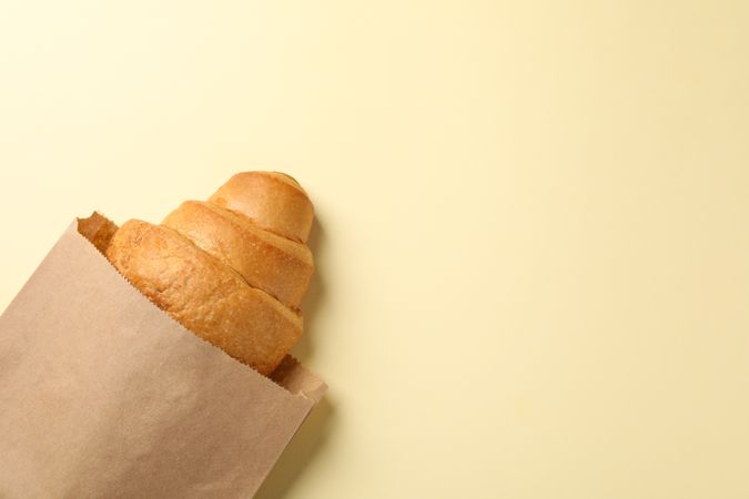Craft paper bag with croissant on beige background, space for text