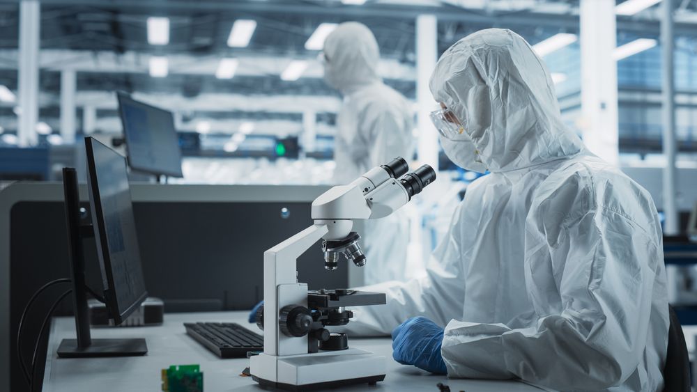 Scientist in hazmat protective suit working at microscope