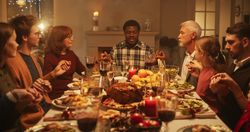 Portrait of a Young Black Man Sitting at a Festive Table with Family and Friends, Praying Before Eating a Turkey Dinner.