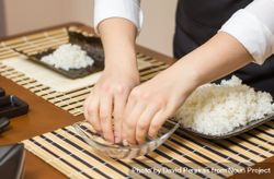 Woman chef wetting fingers to close Japanese sushi rolls with rice on a nori seaweed sheet 47gWg4