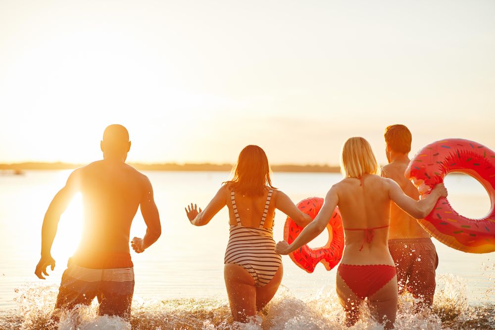 Multi-ethnic group of people running into the lake with floating rings