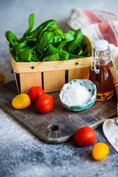 Fresh basil, cherry tomatoes, salt and oil on bread board on kitchen counter