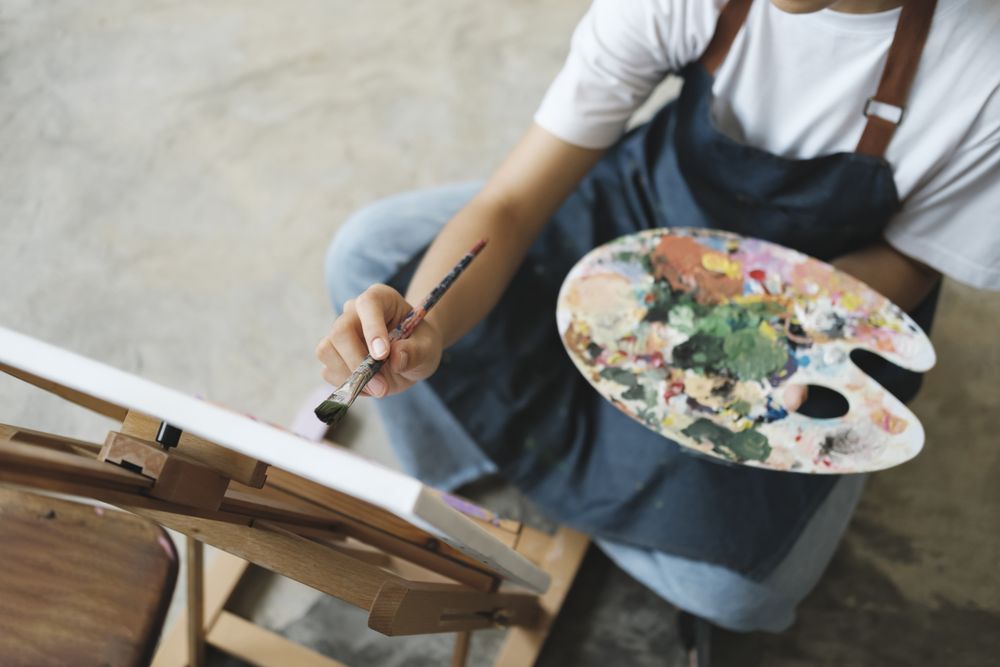 Young Asian female artist painting on canvas doing art projects on her studio.