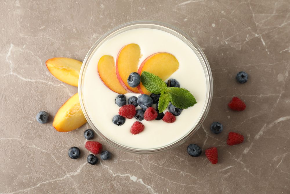 Bowl with sour cream yogurt and fruits on grey background