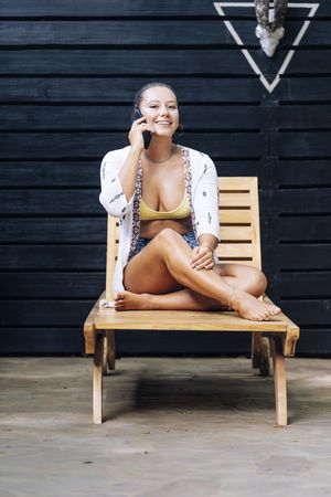 Delighted woman talking on phone while resting on deck chair