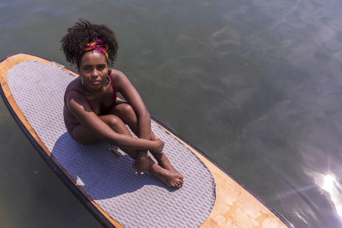 Young Black woman sitting on paddle board in sea